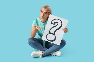 Young woman holding paper with question mark on blue background