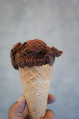 A hand holding of chocolate ice cream in a waffle cone. Close up