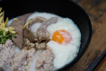 Close up of congee with soft boiled egg and pork entrails in the black bowl for delicious breakfast and clean food in the morning.