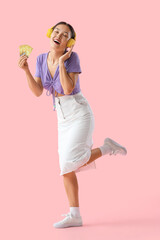 Young Asian woman in headphones with credit cards on pink background