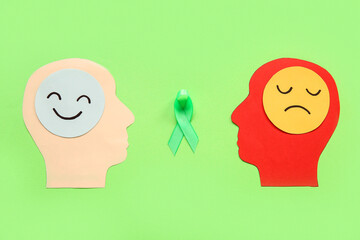 Paper human heads, awareness ribbon and faces with different emotions on green background. Mental Health Day