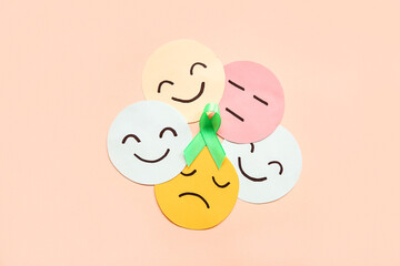 Paper faces with different emotions and green awareness ribbon on pink background. Mental Health Day