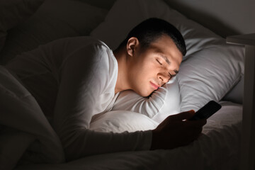 Young man with mobile phone sleeping in bed at night