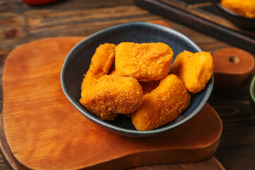 Board with bowl of tasty nuggets on wooden background