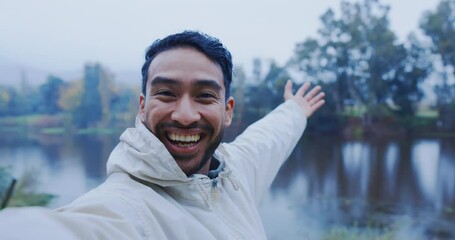 Man, face and video call in nature, rain and lake for outdoor travel, social media influencer and adventure or hiking blog. Content creation, live streaming and Asian person, winter and forest river