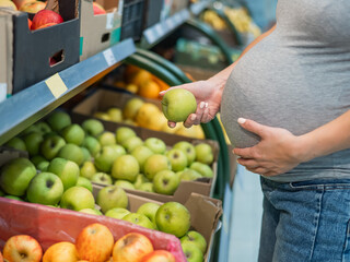 Pregnant woman chooses apples in the store. 