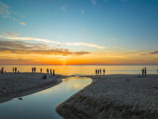 .aerial view of the winding canal on the sandy beach..Tourists watch the sun set beside a small...