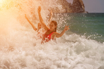 Women ocean play. Seaside, beach daytime, enjoying beach fun. Two women in red swimsuits enjoying themselves in the ocean waves and raising their hands up.