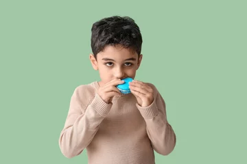 Poster Cute little boy eating tasty macaron on green background © Pixel-Shot