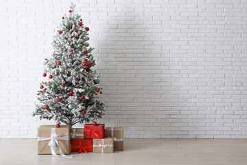 Decorated Christmas tree with gifts against white brick wall