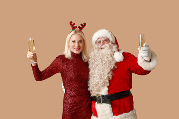 Fototapeta na wymiar Santa Claus and beautiful mature woman in Christmas deer horns with glasses of champagne on brown background