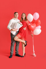 Lovely couple with bouquet of flowers and heart-shaped balloons on red background. Valentine's Day celebration