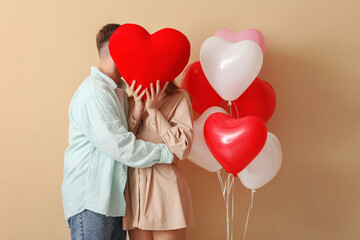 Lovely couple covering face with heart on beige background. Valentine's Day celebration