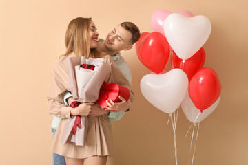 Lovely couple with bouquet of flowers, gift box and heart-shaped balloons on beige background....