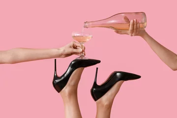 Fotobehang Female legs in high heel shoes with glass and bottle of champagne on pink background. New year party concept © Pixel-Shot