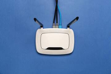 Modern wi-fi router with cables on blue background