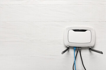 Modern wi-fi router with cables on white wooden background