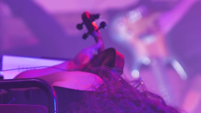 A girl with curly hair is playing the violin. View from behind. Sympho-rock band performing. Close-up of a woman's head and a violin. Slow motion