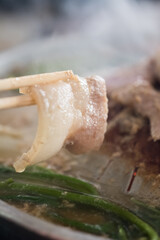 Use chopsticks to pick up the pork belly slices from pot to eat. Focus on the pork belly
