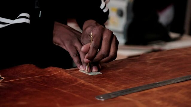 A man uses a stencil to cut out shapes from a large piece of leather to make leather goods
