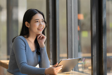 Fototapeta premium A beautiful Asian businesswoman holding a digital tablet while standing in the office room. Business concept.