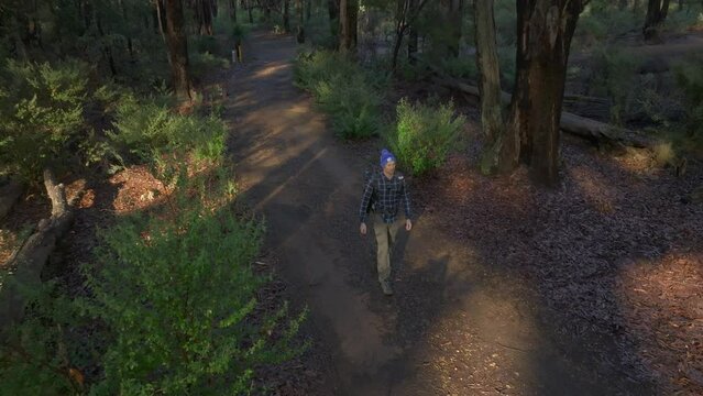 Drone follows man walking through the forest towards camera then pans around as he moves below camera.