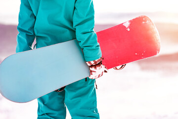 Close up photo of snowboarder holding snowboard in hands and looking at sunset. Ski resort concept