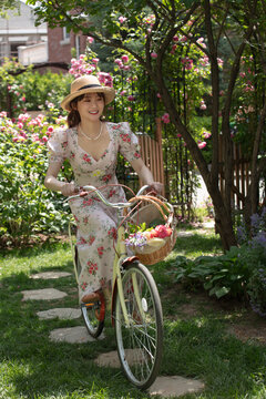 Young and beautiful women ride bicycles in the courtyard full of flowers