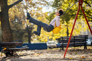 A young trendy woman is swinging on the swing in city park.