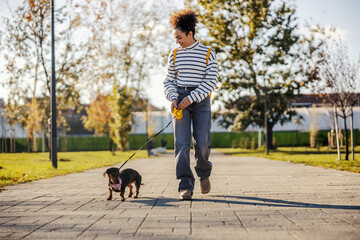 A young fashionable woman is walking her dog on the city street.