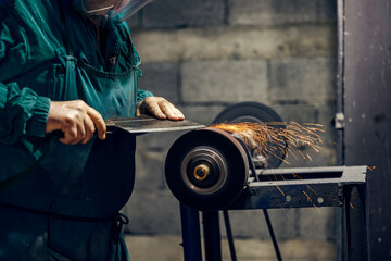Cropped picture of cutler sharpening blade on grindstone in his workshop.