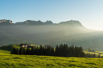 Rural landscape in the Appenzell region with farm houses and meadows in the last light of the evening sun, view to the Alpstein mountains with Saentis, Canton of Appenzell Innerrhoden, Switzerland - Powered by Adobe