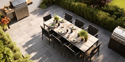 Stylish outdoor kitchen with gas barbecue and dining table set for guests, formal place settings and flowers on paved patio, seen from high angle. - obrazy, fototapety, plakaty