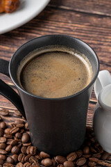 Relaxing americano coffee in black porcelain cup with milk on wooden table