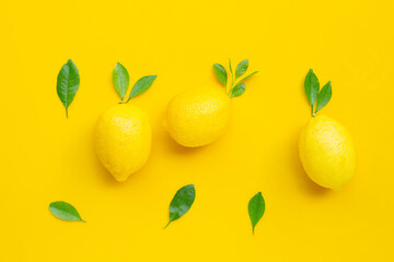 Fresh lemon with green leaves on yellow background.