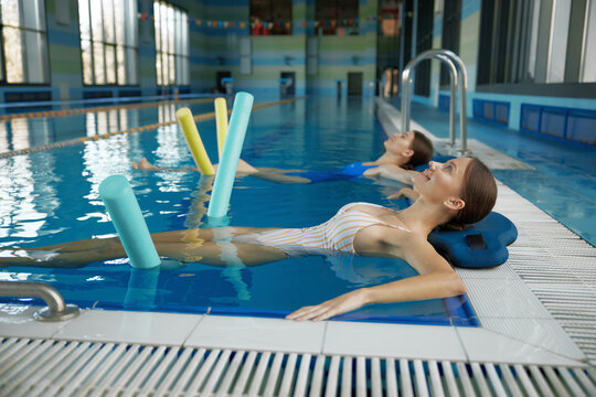 Two women doing relaxing exercise with noodles after training in swimming pool - Powered by Adobe