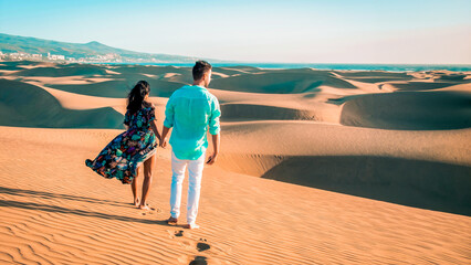 couple walking at the beach of Maspalomas Gran Canaria Spain, men and woman at the dunes desert of Maspalomas Spain Europe in the morning sun - obrazy, fototapety, plakaty
