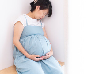 Pregnant woman wearing a blue dress sits down and bears the pain