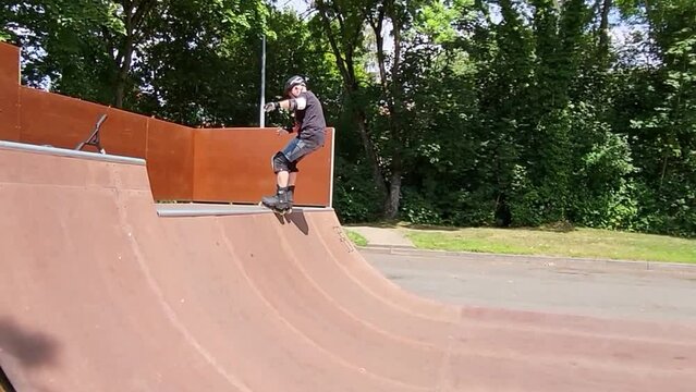 Ein Mann, der mit Inlineskates auf einer Halfpipe in einem Skatepark f&auml;hrt. Der Mann tr&auml;gt einen Helm und f&uuml;hrt einen Trick aus. Die Rampe ist aus Holz und gebogen.