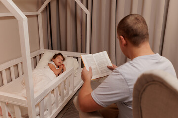 family and education concept - young father reading book to his little daughter lying in bed
