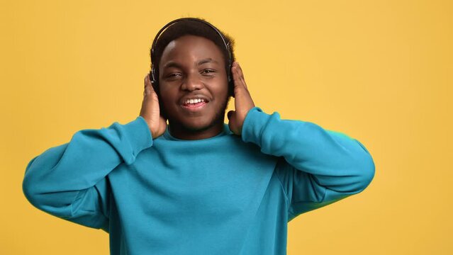 Happy Afro man dancing listening favorite music in headphones posing isolated orange studio closeup