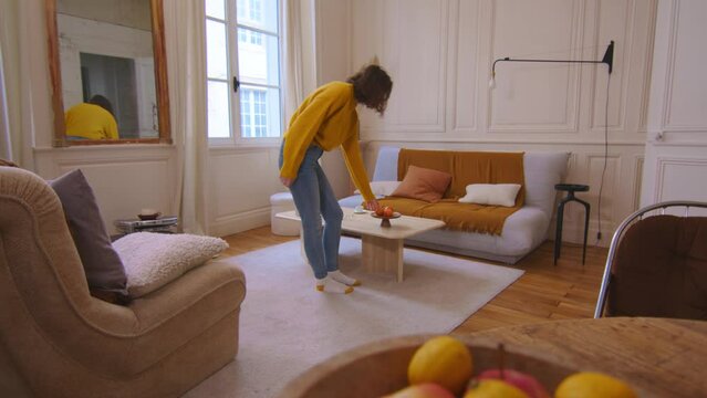 Wide view of living room, female walking and picking up item from coffee table