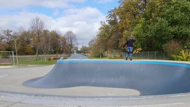 Ein Mann, der mit Inlineskates auf einer Halfpipe in einem Skatepark f&auml;hrt. Der Mann tr&auml;gt einen Helm und f&uuml;hrt einen Trick aus. Die Rampe ist aus Holz und gebogen.
