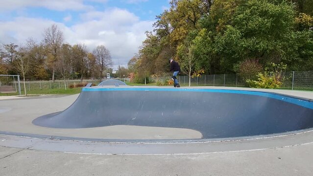 Ein Mann, der mit Inlineskates auf einer Halfpipe in einem Skatepark f&auml;hrt. Der Mann tr&auml;gt einen Helm und f&uuml;hrt einen Trick aus. Die Rampe ist aus Holz und gebogen.
