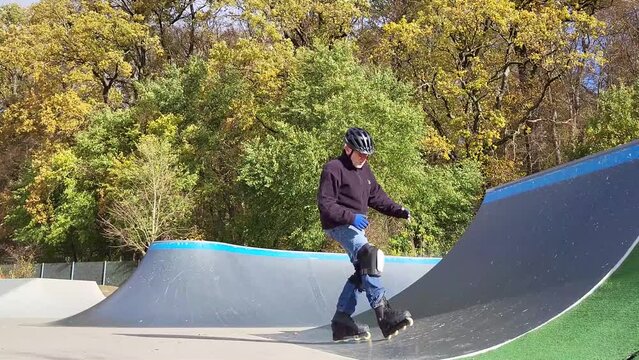 Ein Mann, der mit Inlineskates auf einer Halfpipe in einem Skatepark f&auml;hrt. Der Mann tr&auml;gt einen Helm und f&uuml;hrt einen Trick aus. Die Rampe ist aus Holz und gebogen.