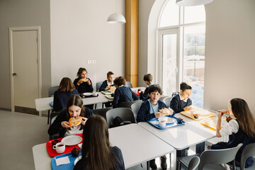 Group of kids eating at table in school cafeteria - Powered by Adobe