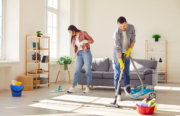 Young happy couple engages in home cleaning, with a vacuum and mop. They demonstrate togetherness...