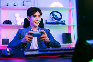 Young positive happy Asian man holding and pressing buttons of a wireless controller playing a...