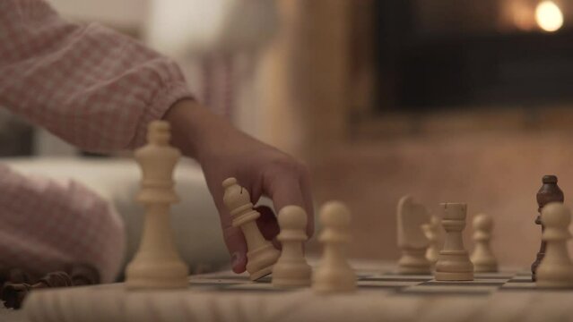 Close-up, child playing chess by the fireplace in the evening