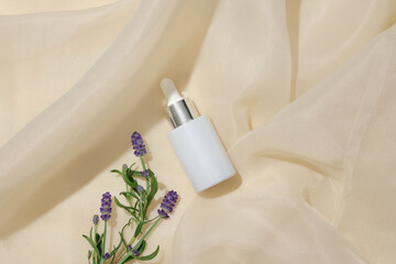 A bottle of white serum and fresh lavender flowers stand out on a beige fabric background. Blank labels for branding and advertising. Lavender essence has the effect of cleansing the skin.